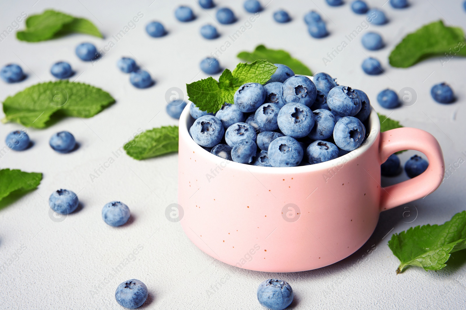 Photo of Cup with juicy blueberries and green leaves on color table