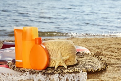 Sun protection products and beach accessories on blanket near sea, space for text