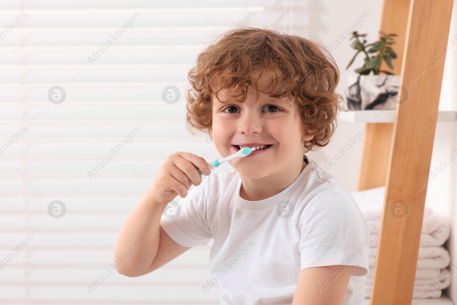 Photo of Cute little boy brushing his teeth with plastic toothbrush in bathroom, space for text