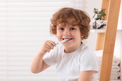 Cute little boy brushing his teeth with plastic toothbrush in bathroom, space for text