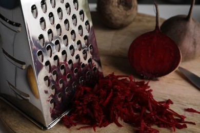 Photo of Grater and fresh ripe beetroot on wooden board, closeup
