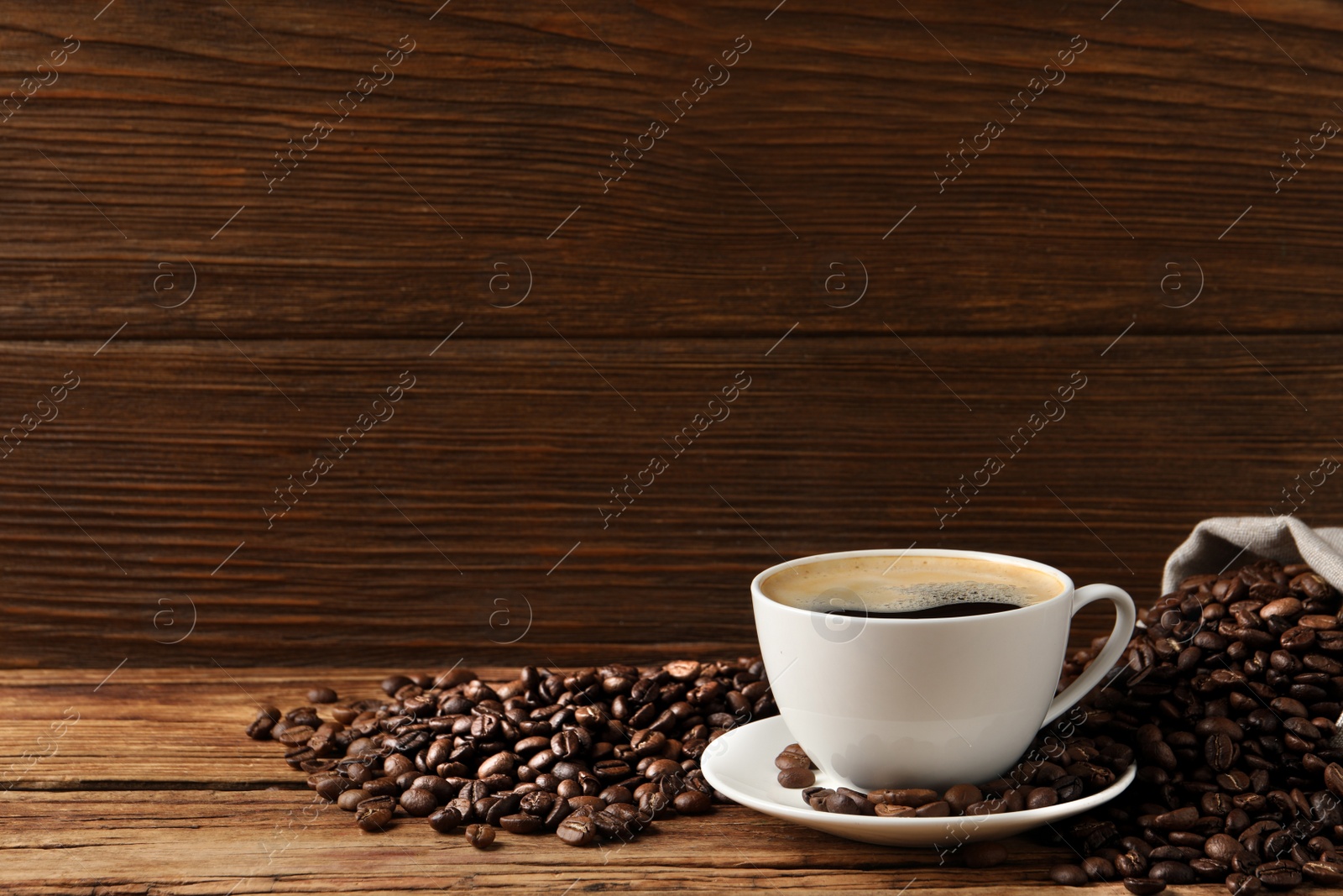 Photo of Cup of aromatic hot coffee and beans on wooden table, space for text