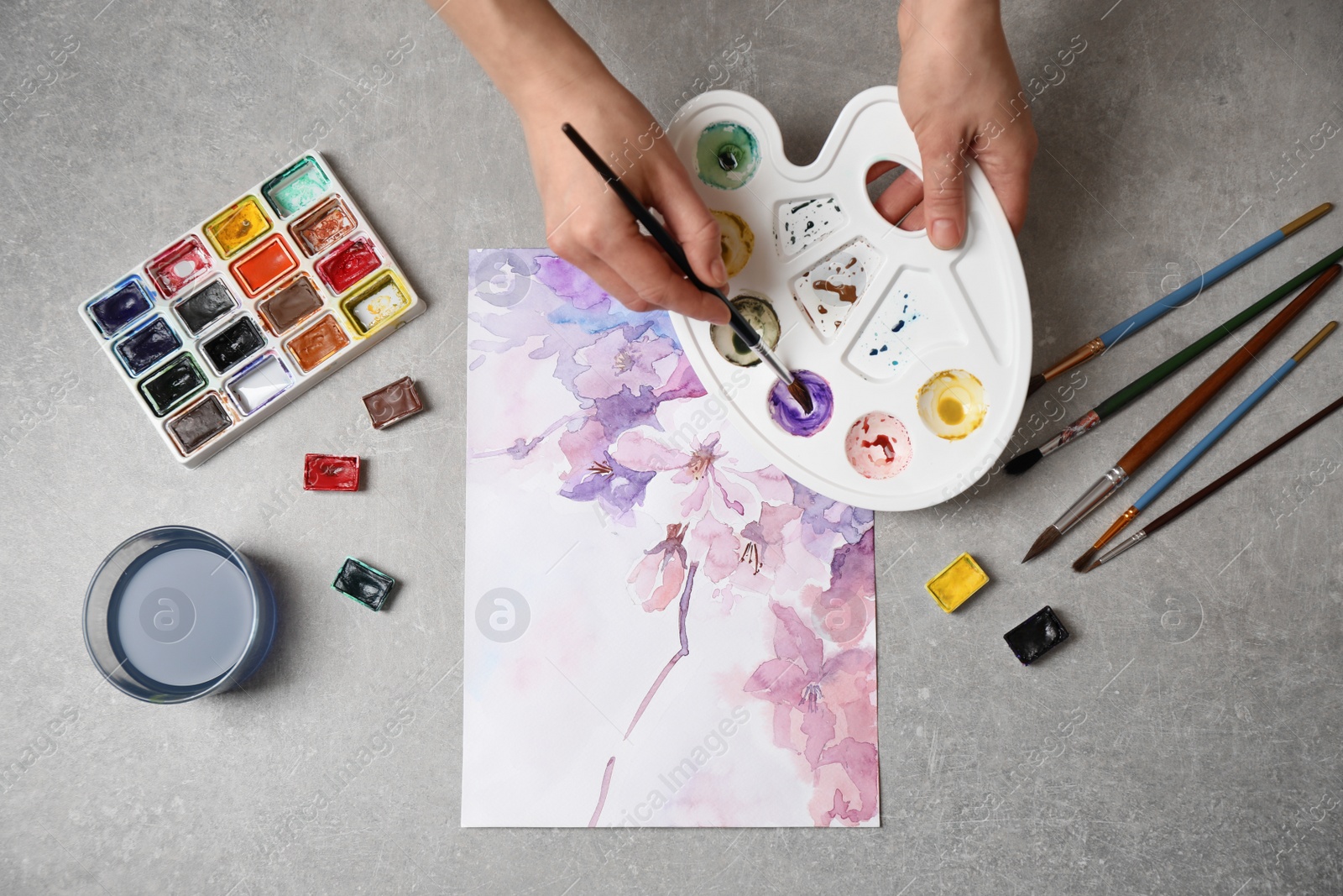 Photo of Woman painting flowers with watercolor at grey stone table, top view