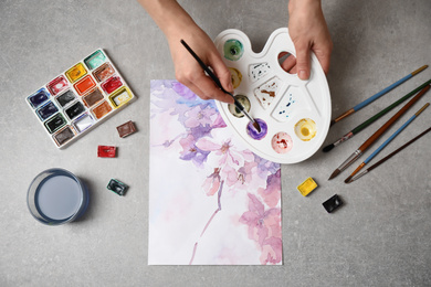 Woman painting flowers with watercolor at grey stone table, top view