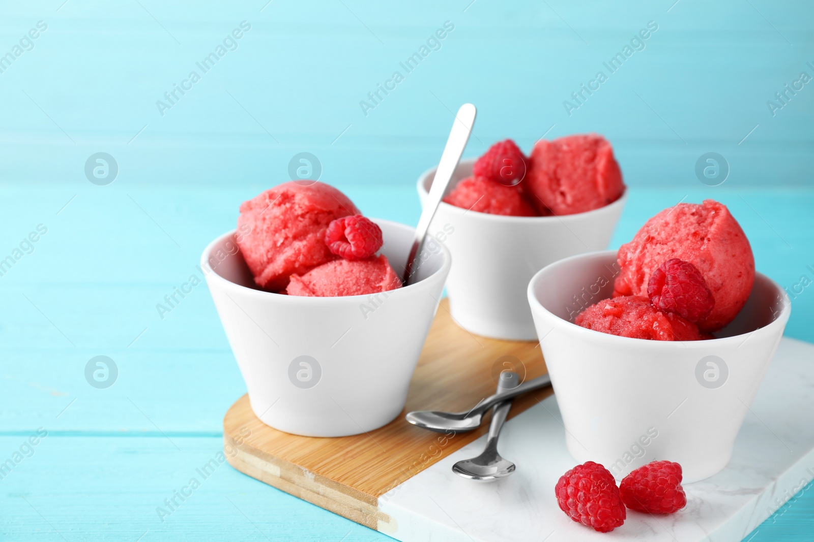Photo of Bowls with delicious raspberry ice cream on light blue wooden table