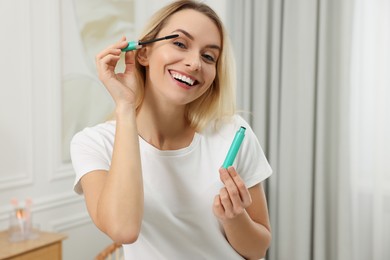 Photo of Beautiful happy woman applying mascara at home