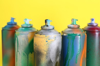 Photo of Many spray paint cans on yellow background, closeup