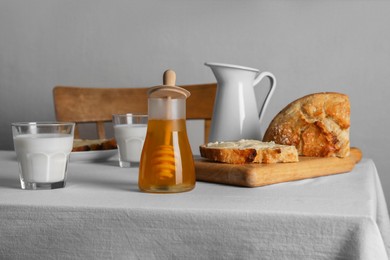 Photo of Delicious honey, milk and bread with butter served for breakfast on table indoors