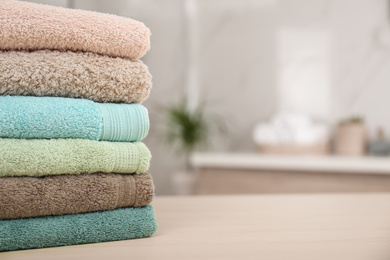 Photo of Stack of fresh towels on wooden table in bathroom, closeup. Space for text