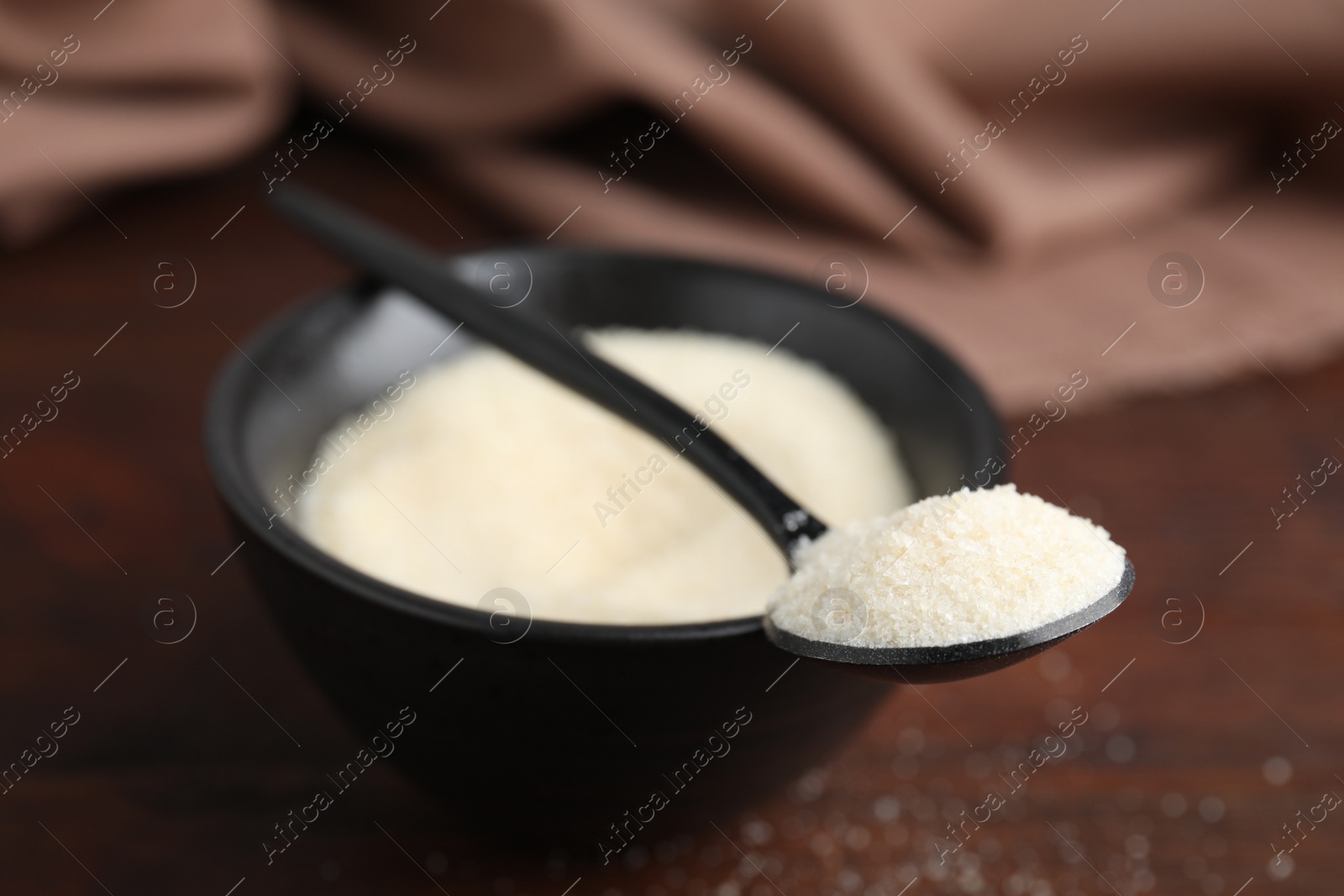 Photo of Gelatin powder in bowl and spoon on table, closeup