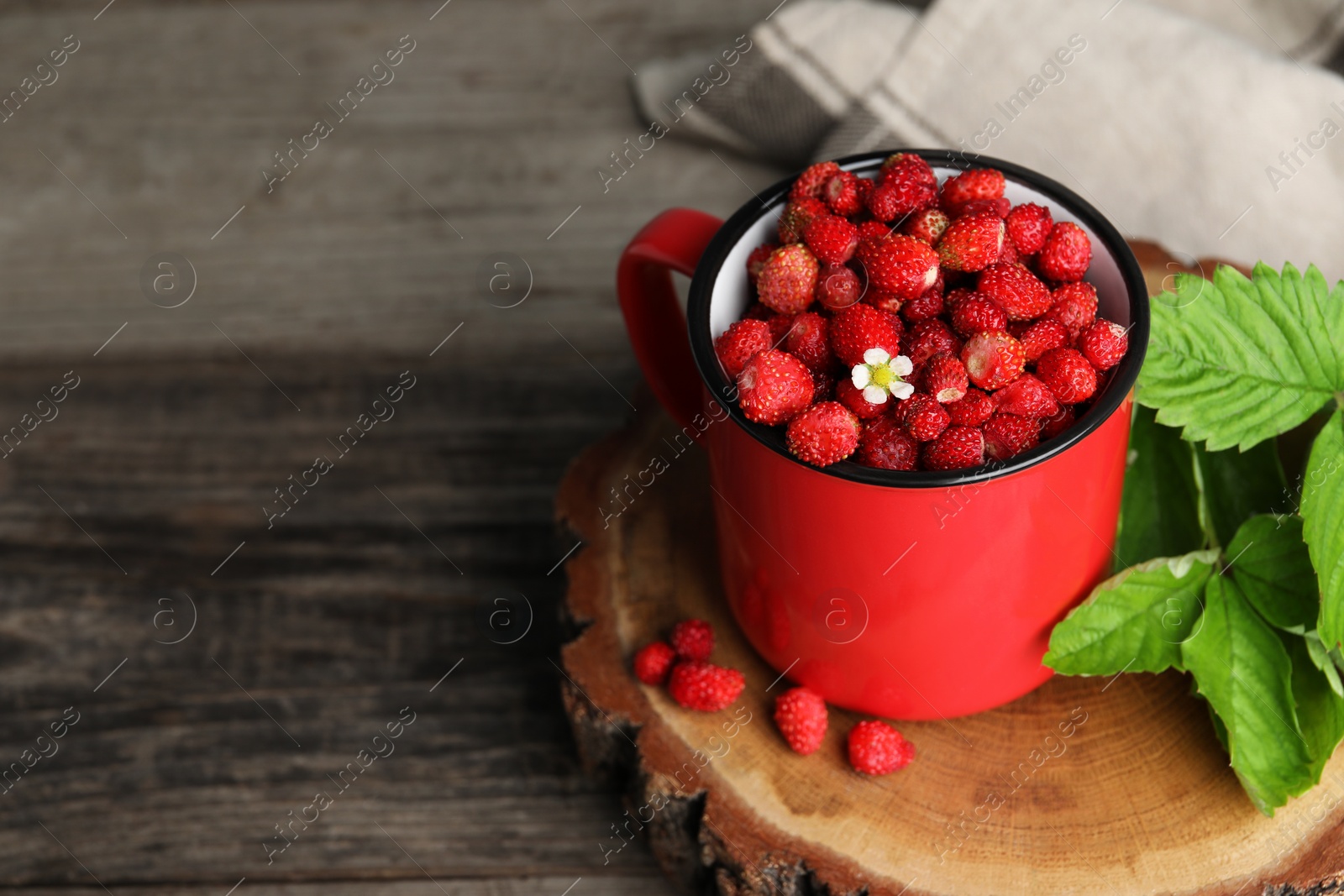 Photo of Fresh wild strawberries in mug and leaves on wooden table. Space for text