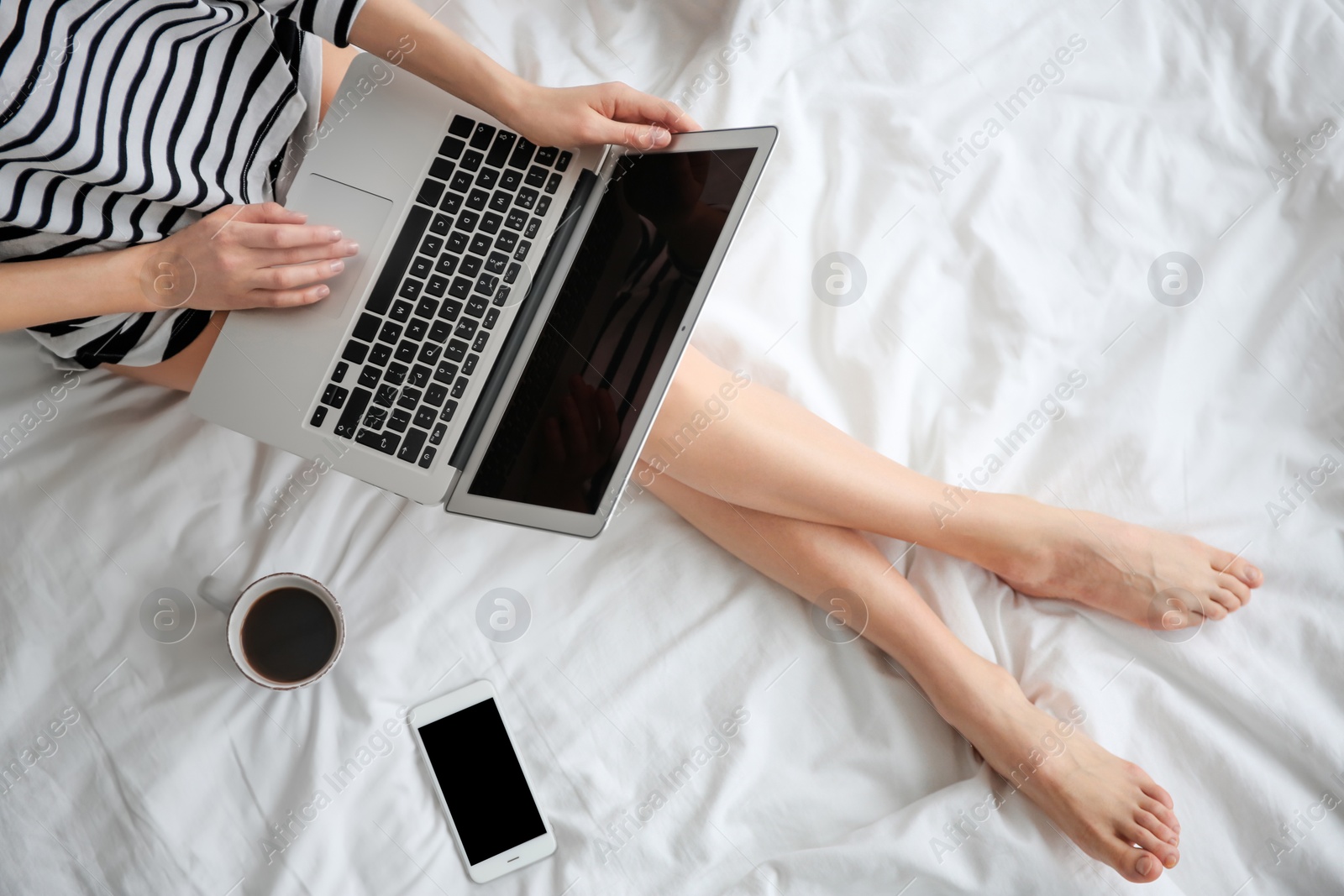 Photo of Female blogger with laptop and cup of coffee on bed, top view