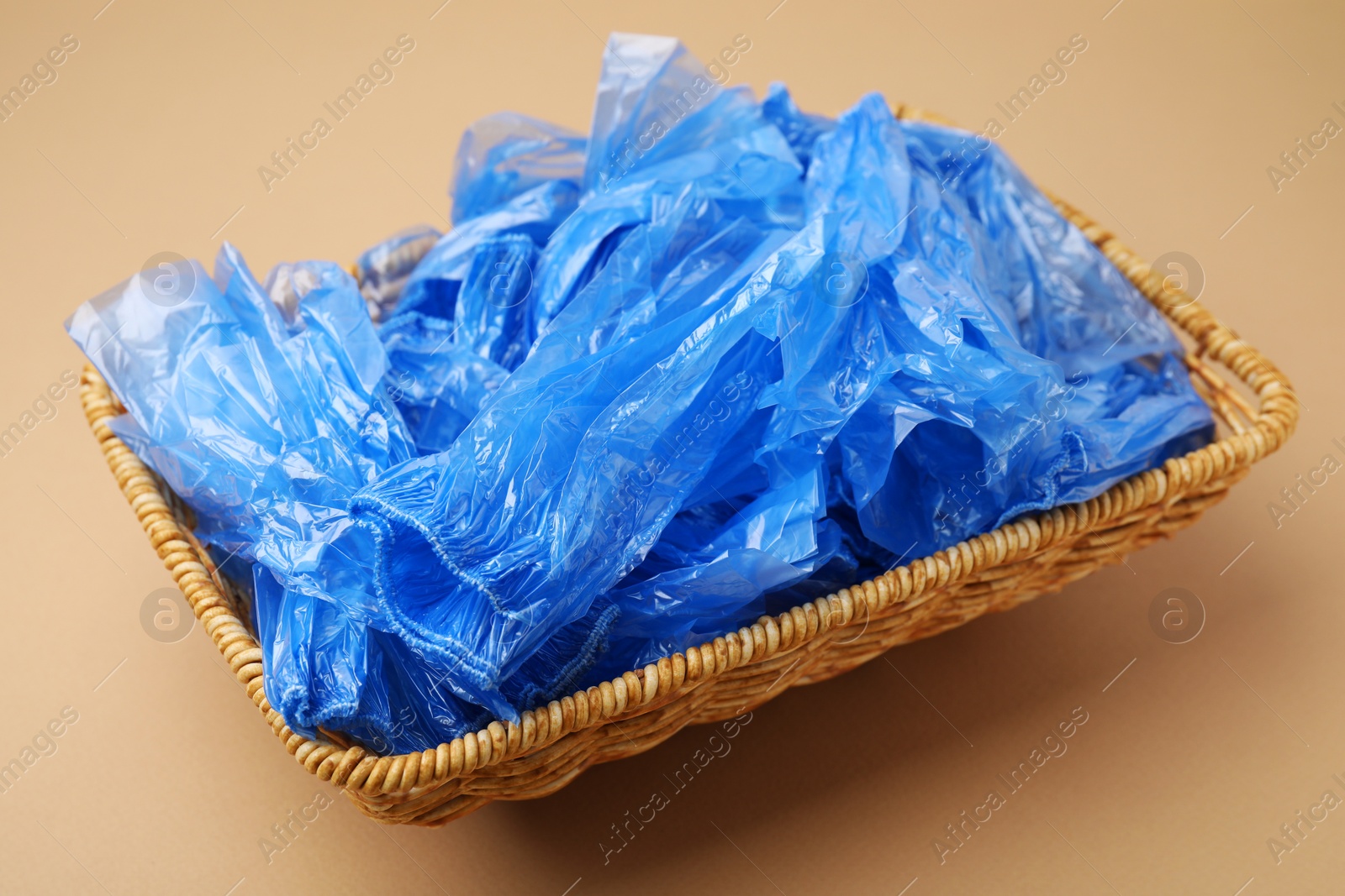 Photo of Blue medical shoe covers in wicker basket on beige background, closeup