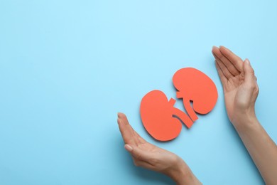 Woman protecting paper cutout of kidneys on light blue background, top view. Space for text