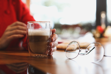 Woman with fresh morning coffee at table in cafe, closeup