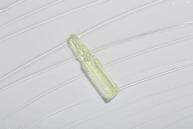 Photo of Skincare ampoule on white surface covered with gel, top view