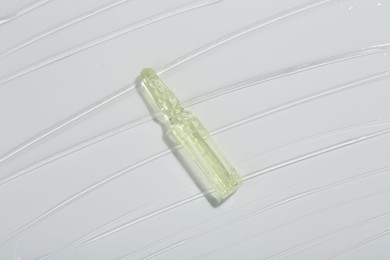 Skincare ampoule on white surface covered with gel, top view