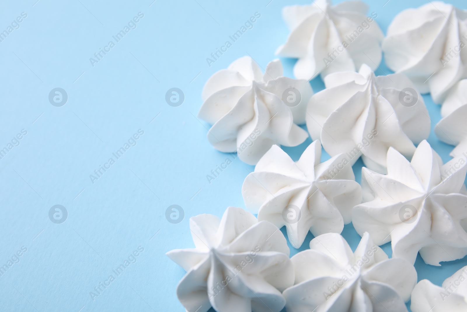 Photo of Tasty meringue cookies on light blue background, closeup. Space for text