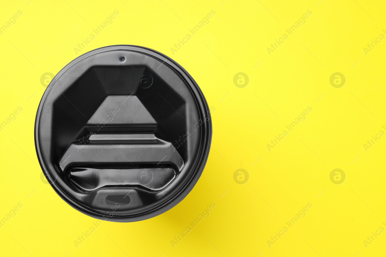 Photo of One paper cup with black lid on yellow background, top view with space for text. Coffee to go