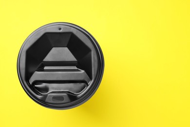 One paper cup with black lid on yellow background, top view with space for text. Coffee to go