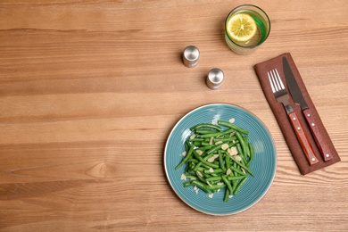 Plate with tasty green beans and almonds on wooden table, top view