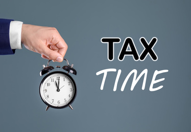 Image of Time to pay taxes. Man holding clock on grey background, closeup