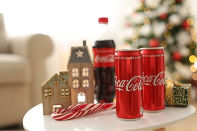 MYKOLAIV, UKRAINE - JANUARY 15, 2021: Coca-Cola cans and bottle near gift box on table with Christmas decor