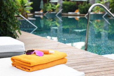 Beach towels, sunglasses and sunscreen on sun lounger near outdoor swimming pool, space for text. Luxury resort