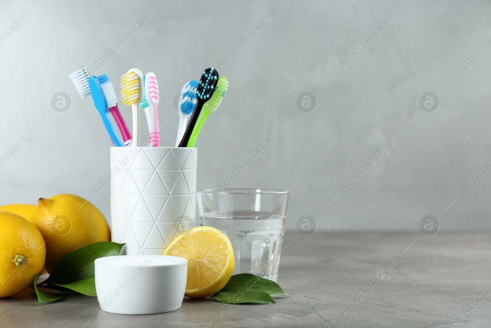 Photo of Toothbrushes, lemons and bowl of baking soda on grey table, space for text