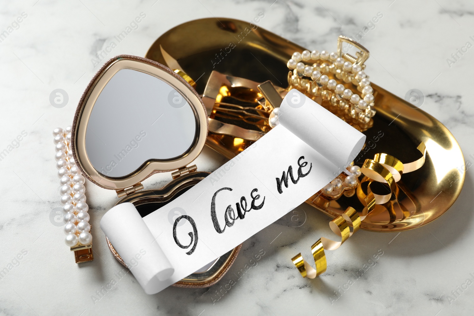 Photo of Paper with handwritten phrase I Love Me, mirror and hair accessories on table, closeup