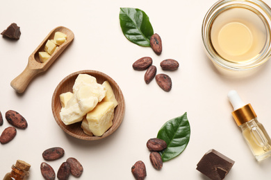 Organic cocoa butter, beans and essential oil on beige background, flat lay