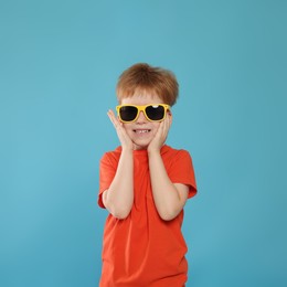 Cute little boy with sunglasses on light blue background