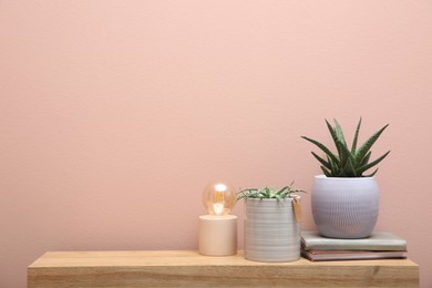 Photo of Beautiful potted plants, lamp and books on wooden table near pink wall, space for text. Interior accessories