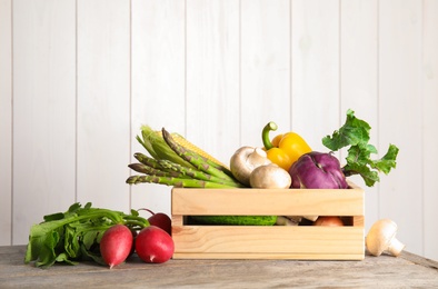 Crate with assortment of fresh vegetables on table against light background. Space for text