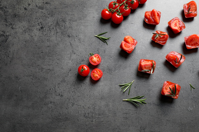 Photo of Ice cubes with tomatoes and rosemary on grey table, flat lay. Space for text