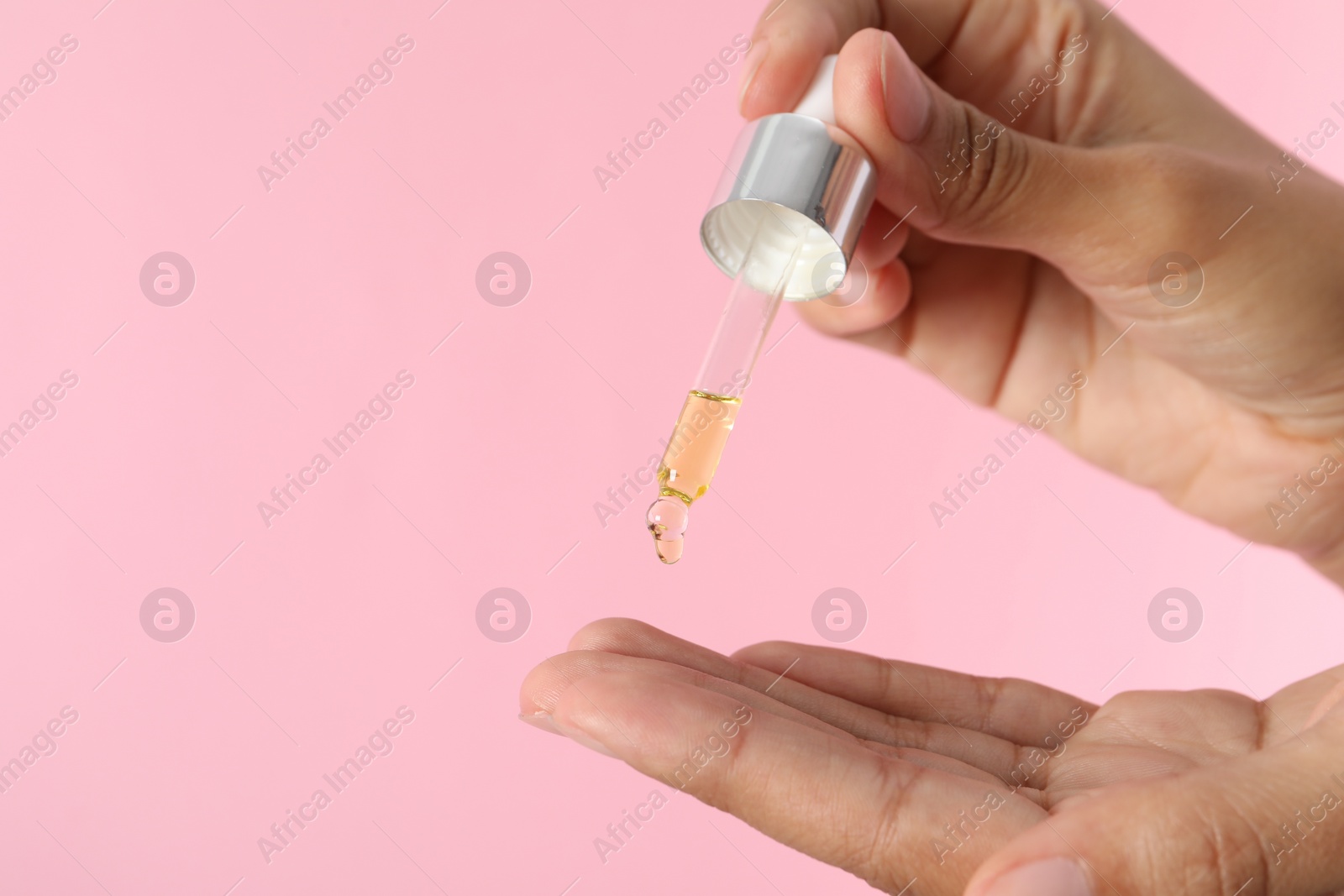 Photo of Woman applying cosmetic serum onto her finger on pink background, closeup. Space for text