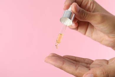 Woman applying cosmetic serum onto her finger on pink background, closeup. Space for text