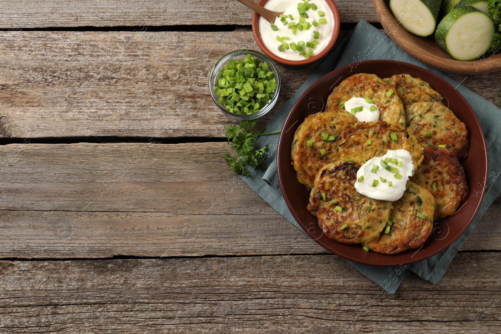 Photo of Delicious zucchini pancakes with sour cream served on wooden table, flat lay. Space for text