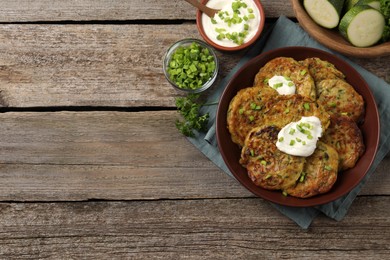 Photo of Delicious zucchini pancakes with sour cream served on wooden table, flat lay. Space for text