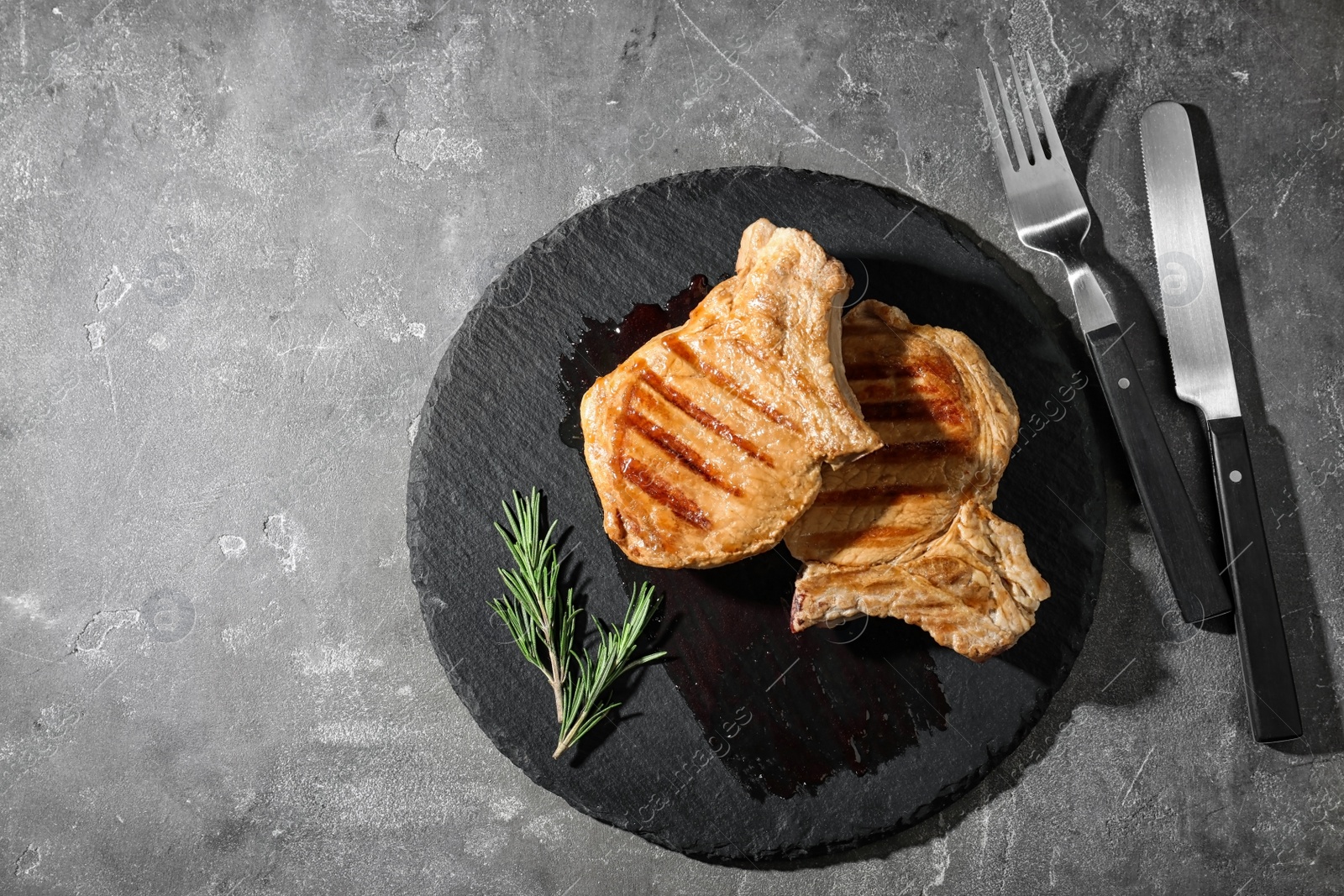 Photo of Slate plate with grilled meat on grey background, top view. Space for text