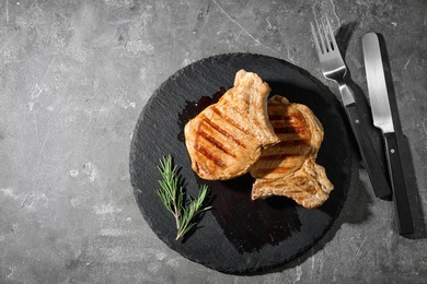 Photo of Slate plate with grilled meat on grey background, top view. Space for text