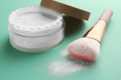 Photo of Rice loose face powder and makeup brush on turquoise background, closeup