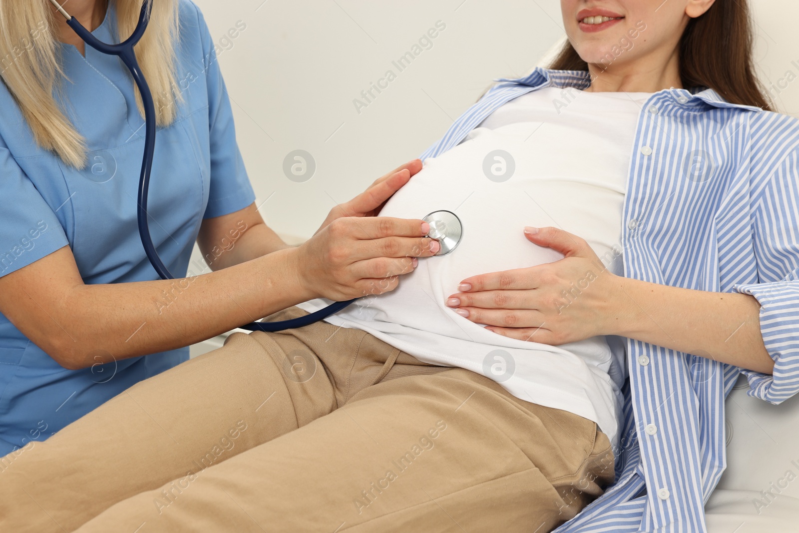 Photo of Pregnancy checkup. Doctor with stethoscope listening baby's heartbeat in patient's tummy in clinic, closeup