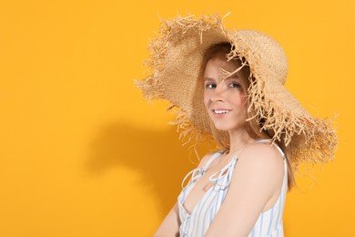 Beautiful young woman in straw hat on orange background, space for text