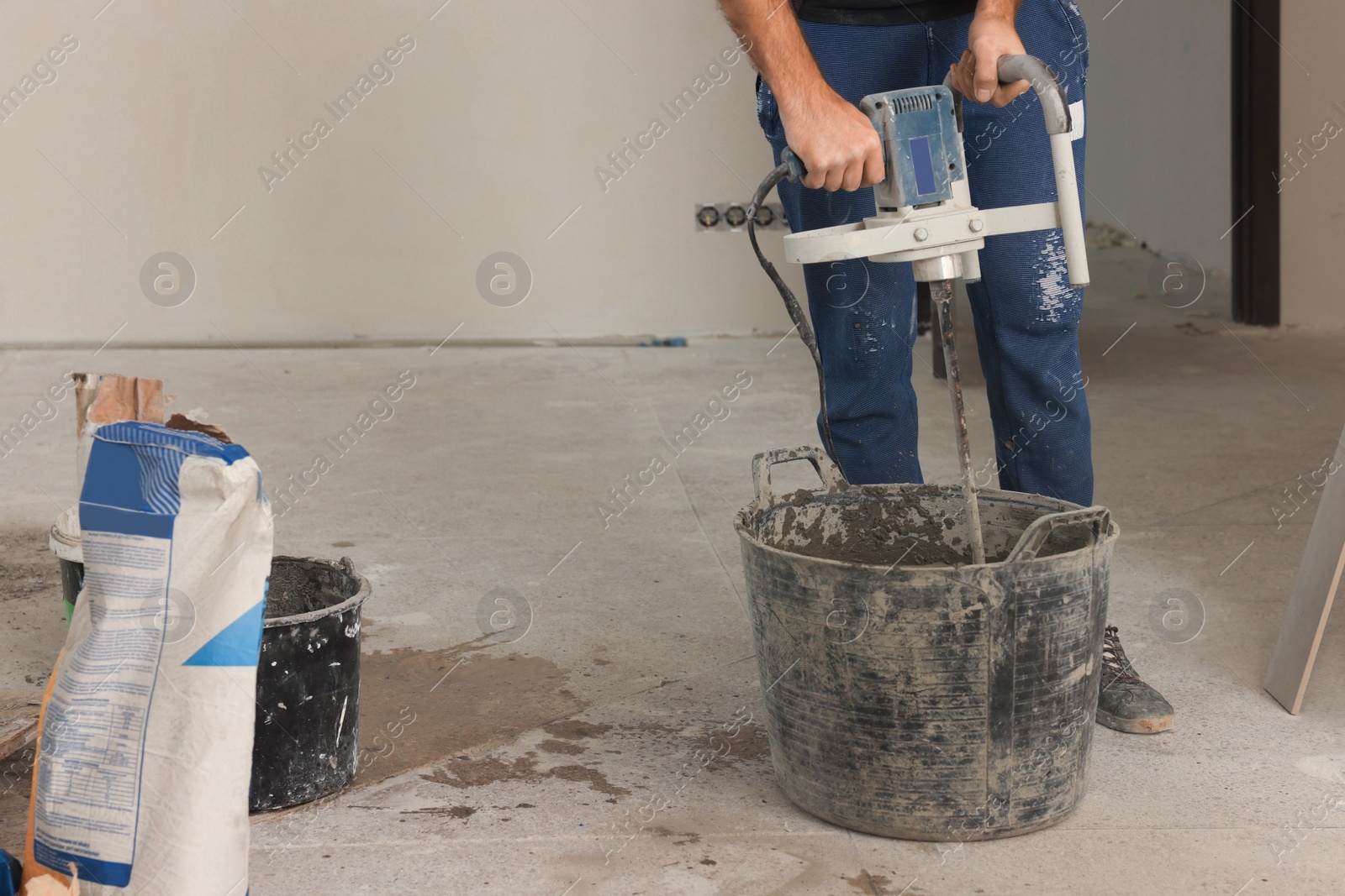 Photo of Professional worker mixing cement in bucket indoors, closeup. Tiles installation process