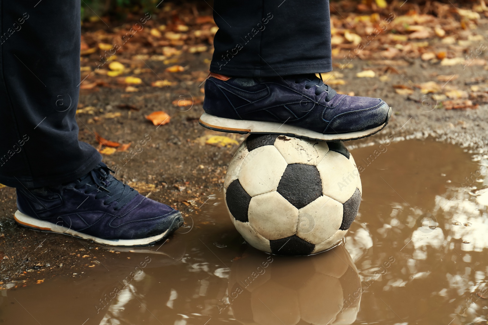 Photo of Man with soccer ball in muddy puddle outdoors, closeup