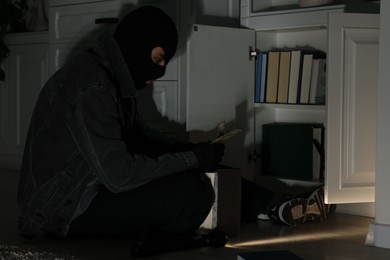 Photo of Thief stealing money near chest of drawers at foreign house. Burglary