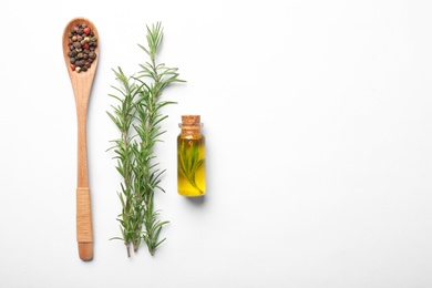 Bottle of rosemary oil, wooden spoon with spices and fresh twigs on white background, top view