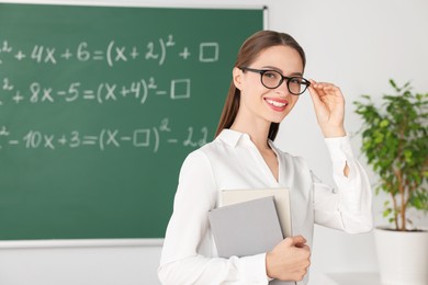Portrait of young math’s teacher near chalkboard in classroom