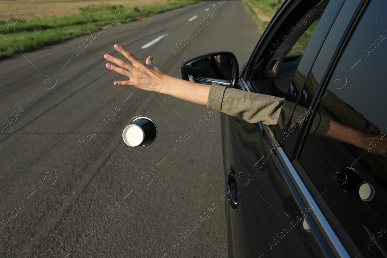 Photo of Driver throwing away paper cup from car window. Garbage on road